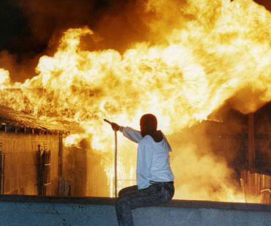 A resident vainly attempts to fight a raging fire at 79th Street and Normandie Avenue using a garden hose. (April 29, 1992) Source: Mike Meadows / Los Angeles Times